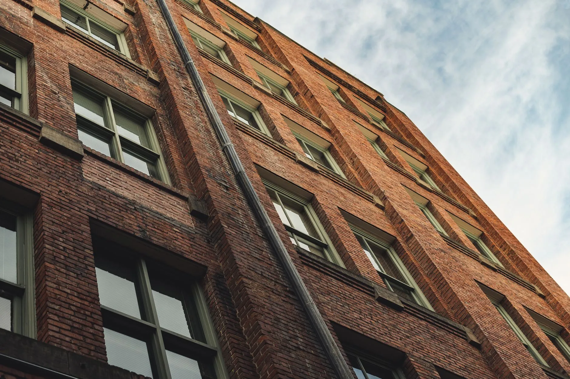 Tall red brick tenement seen from below, deep window reveals and a rainwater pipe running up the facade.