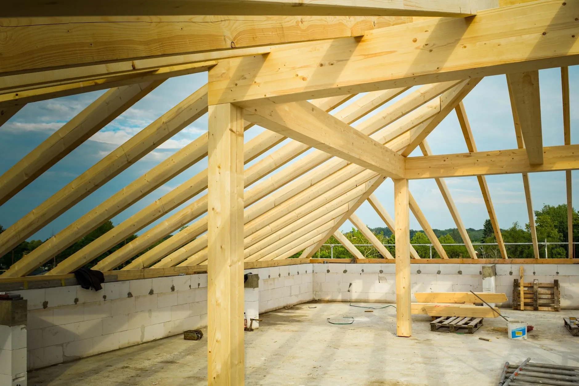 Timber rafters and a central post seen from inside the unfinished shed, blockwork walls and sky beyond.