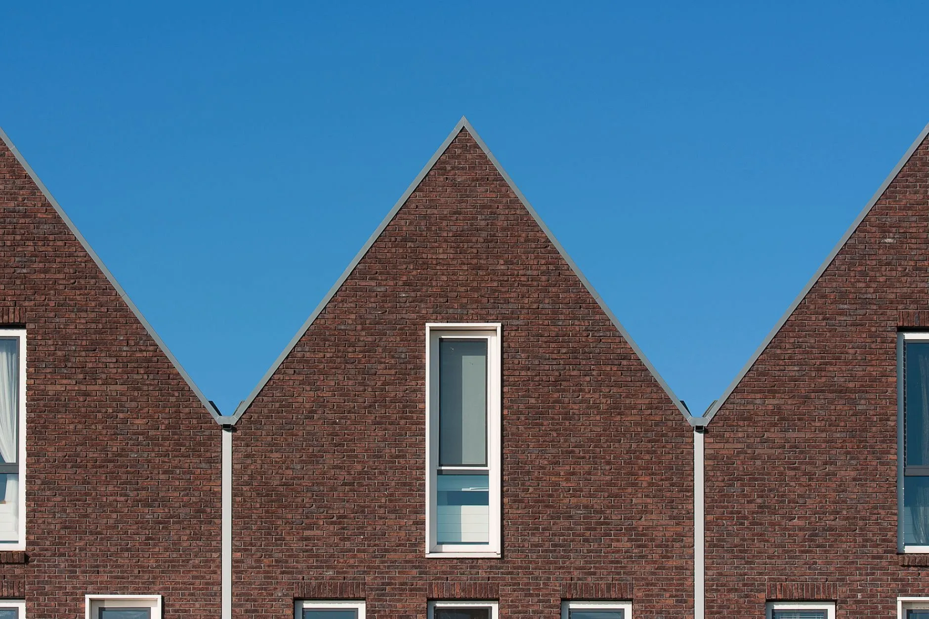 Three steep brick gables in a row against a clear blue sky, one tall window in the middle gable.