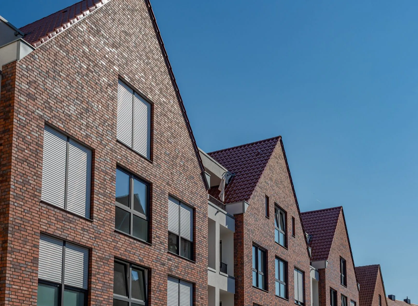 Brick apartment gables stepping down a street, white roller blinds on the windows.