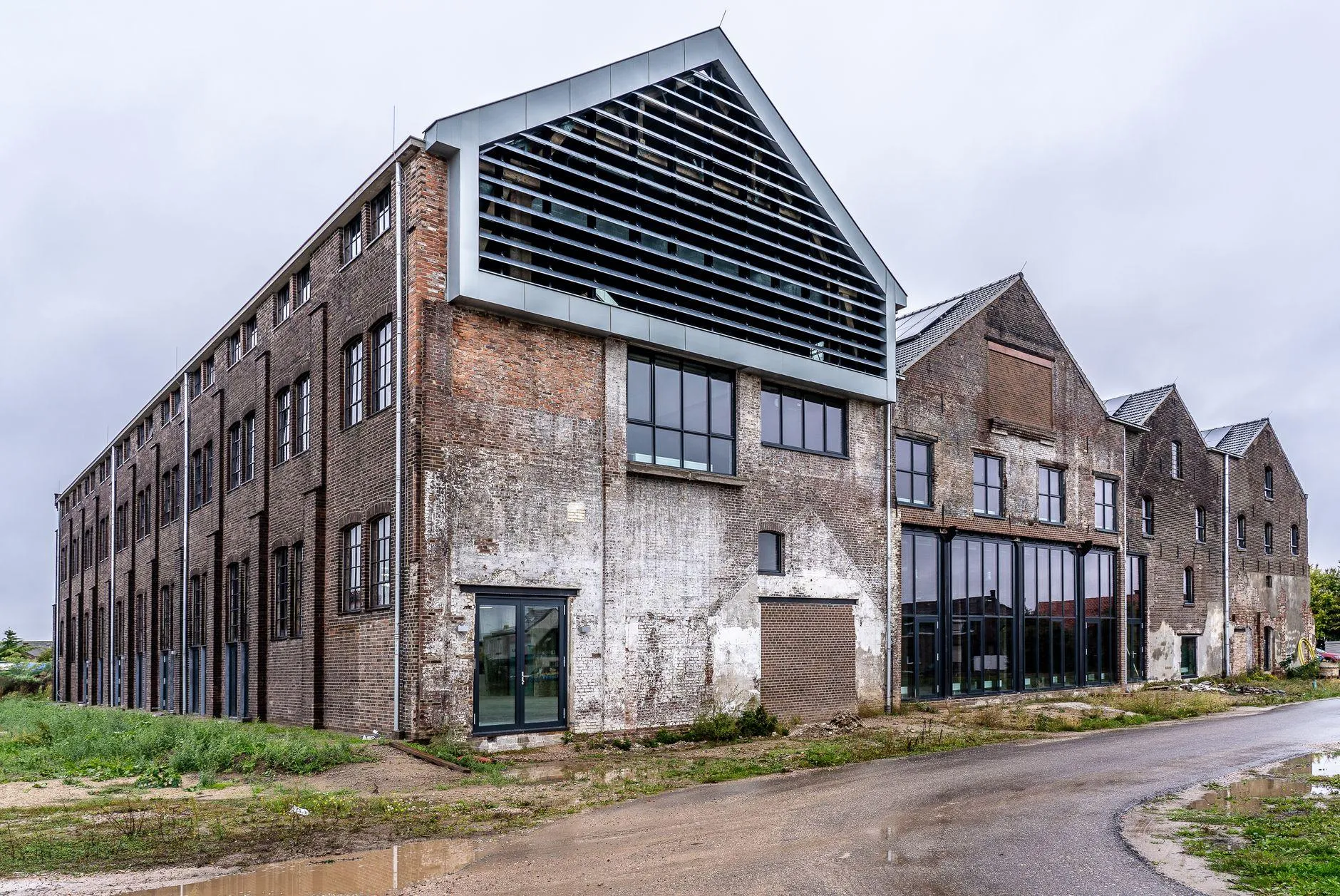 Long brick shed with a weathered facade, a new louvred gable in grey metal and black-framed glazing at ground floor.