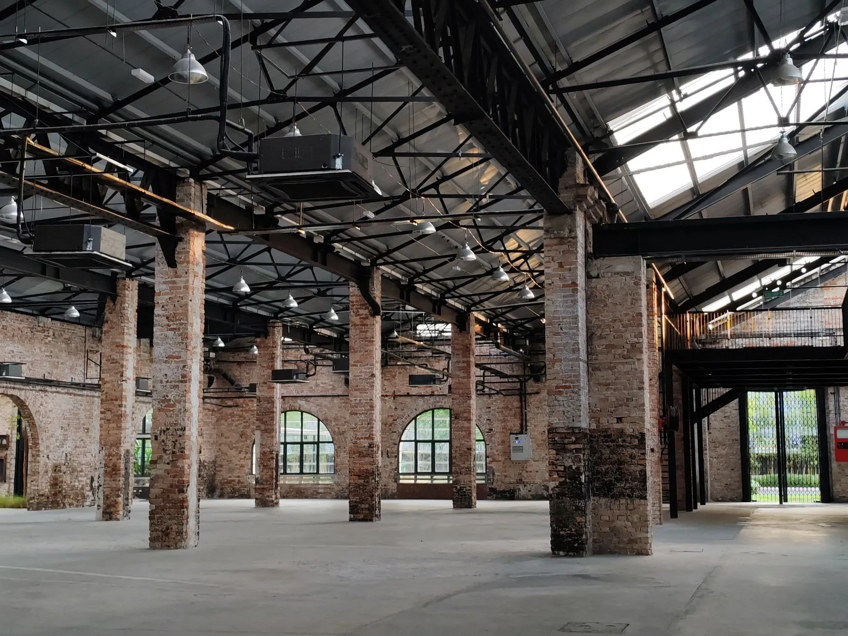 Tall industrial hall with old brick piers, a black steel roof structure and arched windows at the far end.